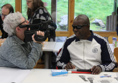A student film maker films one of the delegates at the conference who is visually impaired. They are laughing and chatting together.