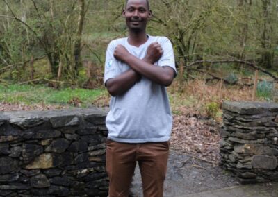 A delegate is outside next to a dry stone wall, he is signing "Love" in ASL
