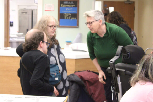 A facilitator at the conference talks to a disabled young person who has just arrived with his mother.