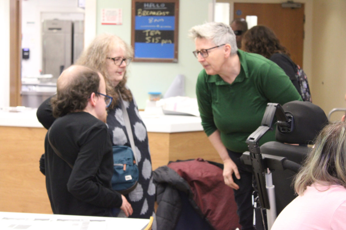 A facilitator at the conference talks to a disabled young person who has just arrived with his mother.
