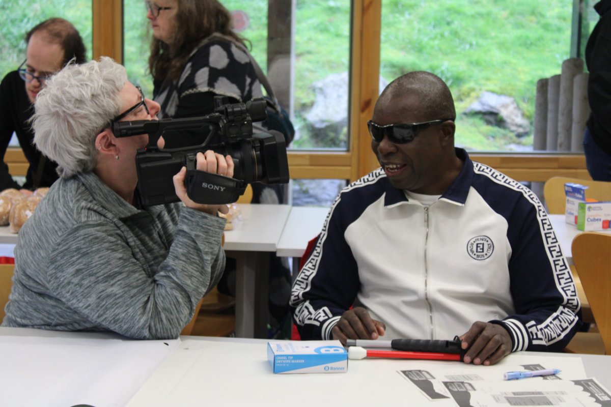 A student film maker films one of the delegates at the conference who is visually impaired. They are laughing and chatting together.